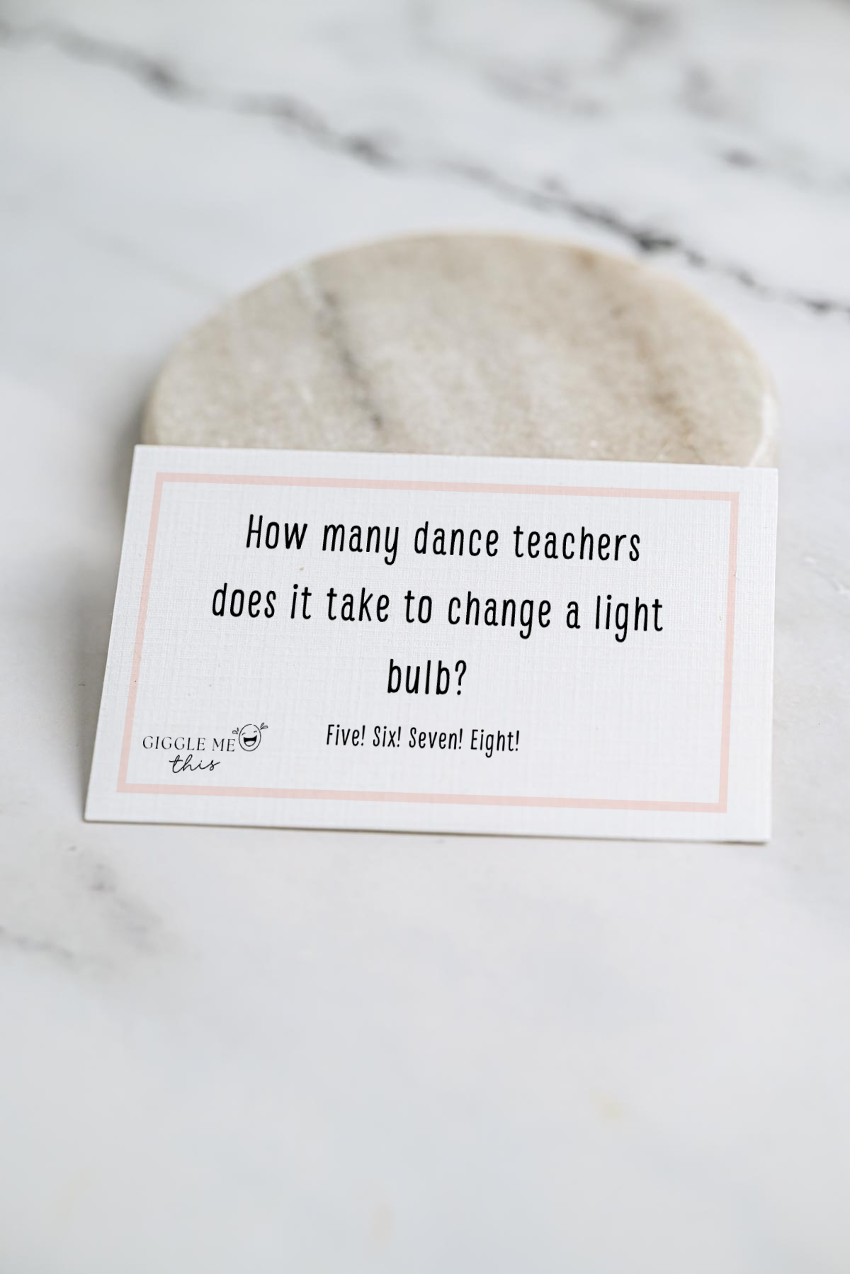 A card on a marble surface reads: “How many dance teachers does it take to change a light bulb? Five! Six! Seven! Eight!”—one of the classic jokes about dance.
